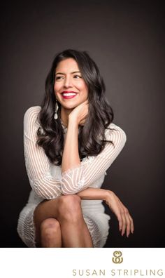 a woman sitting on top of a chair with her hand under her chin and smiling at the camera