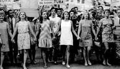 a group of women standing next to each other in front of a crowd holding signs