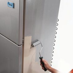 a person painting the side of a refrigerator with a roller on it's handle