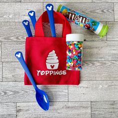 a red bag with spoons, sprinkles and candy in it sitting on a wooden floor