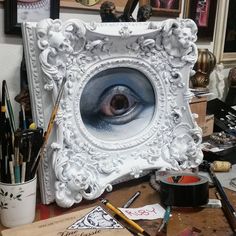 an eye is seen in the center of a white frame surrounded by art supplies and other items