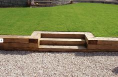 a wooden bench sitting on top of a gravel field next to a lush green park