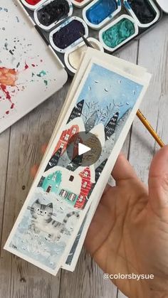 someone is holding an art card in their hand and painting it with watercolors