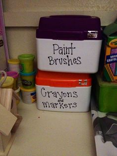 three plastic containers with words painted on them sitting next to other craft supplies and toys