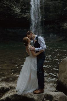 a bride and groom kissing in front of a waterfall