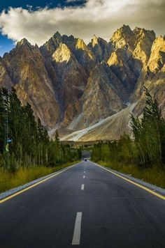 an empty road with mountains in the background and trees on both sides, under a cloudy sky