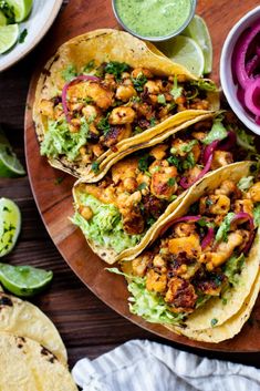 three tacos on a plate with guacamole, onions and cilantro