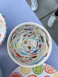 two bowls with different designs on them sitting on a table next to plates and cups