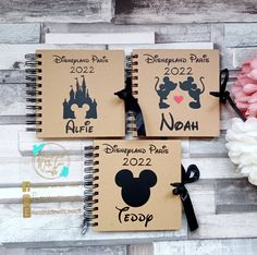 two spiral notebooks with mickey mouse and disneyland parks on them, next to a flower