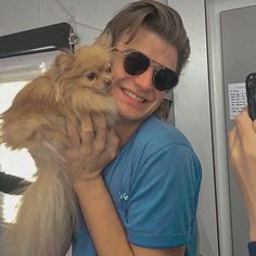 a man is holding a small dog and taking a selfie with his cell phone