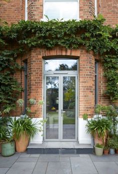 an entrance to a brick building with potted plants on the outside and glass doors