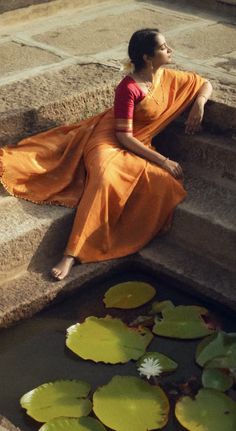 a woman in an orange dress sitting on steps next to water lillies and lily pads