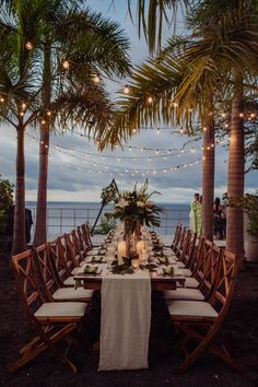 an outdoor dining table set up with candles and greenery on the tables under palm trees