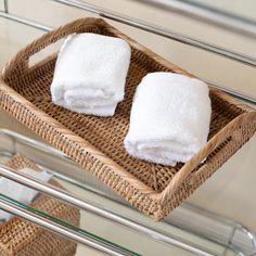 two white towels sitting in a basket on top of a towel rack next to a glass shelf