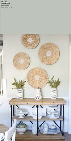 three wicker baskets hanging on the wall above a wooden table with plates and bowls