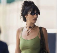 a woman in a green tank top is walking down the street with her hand on her hip