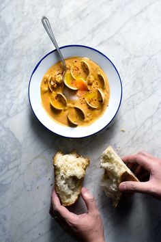 two hands holding pieces of bread over a bowl of soup