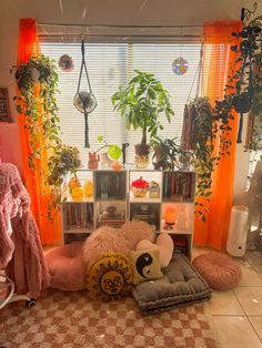 a living room filled with lots of plants next to a window covered in orange curtains