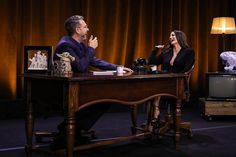 two people are sitting at a desk and one is giving the peace sign with her hand