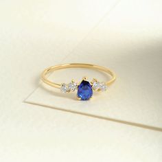 a yellow gold ring with three diamonds and a blue stone on the side, sitting on a white surface