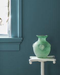 a green vase sitting on top of a white stand in front of a blue wall