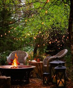 a fire pit surrounded by wicker chairs and lanterns in the woods with string lights