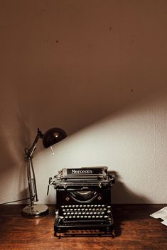 an old fashioned typewriter sitting on top of a wooden table next to a lamp