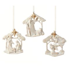 three white christmas ornaments hanging from candles with nativity scene in the middle and star on top