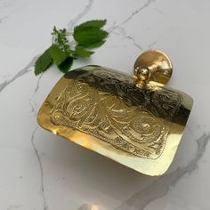 a gold flask on a marble surface with a green plant in the background,