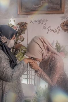 two women in hijabs are touching each other's hands while standing next to a sign