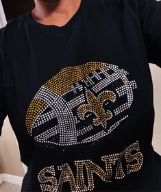 🏈 Elevate Your Game Day Style With Our New Orleans Saints Rhinestone Black T-Shirt! Our 100% cotton black t-shirt with a dazzling New Orleans Saints rhinestone decal is the must-have addition to your fan wardrobe. Designed for ultimate comfort and style, this shirt is perfect for die-hard Saints fans who want to make a statement.🌟 Key Features That Will Win You Over: 🌟✨ Sparkling Rhinestone Brilliance: The centerpiece of this stunning t-shirt is the New Orleans Saints rhinestone decal that adds a touch of glamour and shimmer to your game-day look. Whether you're at the stadium or cheering from home, you'll shine bright and steal the spotlight.✨ Unmatched Comfort: Crafted from 100% premium cotton, our t-shirt offers unrivaled comfort that'll keep you at ease throughout the game. No more Rhinestone Decal, New Orleans Saints, Scarf Styles, Black Tshirt, New Orleans, Fashion Rings, Leggings, Wardrobe, T Shirt