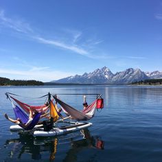 two people sitting in hammocks on a boat with mountains in the background and water