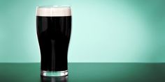 a glass of dark beer sitting on top of a green table next to a blue wall