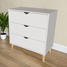 a white dresser sitting on top of a hard wood floor next to a potted plant