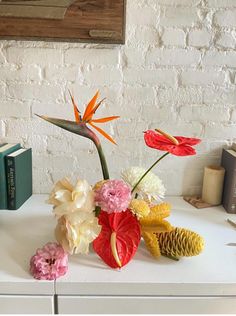 some flowers are sitting on a table next to books and a vase with an orange flower in it