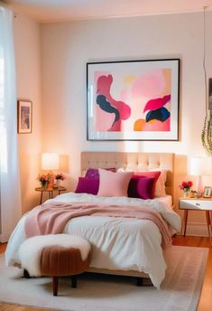 a white bed with pink and purple pillows in a bedroom next to a painting on the wall