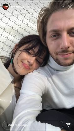 a man and woman laying next to each other in front of a white net fence