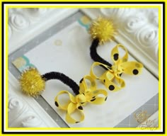 two yellow and black hair bows with pom - poms in front of a white frame