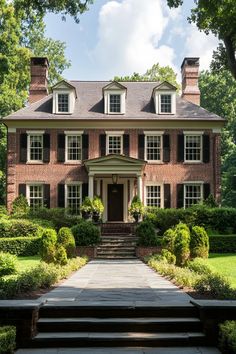 a large brick house surrounded by lush green trees and shrubbery with steps leading up to the front door