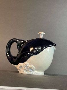 a black and white vase with a dolphin on it's side sitting on a shelf