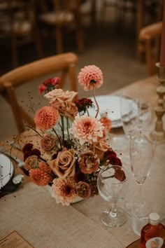 an arrangement of flowers on a table with empty wine glasses and place settings for dinner