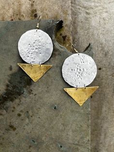 two gold and silver earrings on top of a stone slab, one with an upside down design