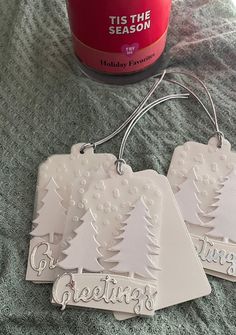 two white christmas tags sitting on top of a bed next to a jar of seasoning