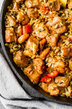 a skillet filled with chicken and rice on top of a table next to a napkin