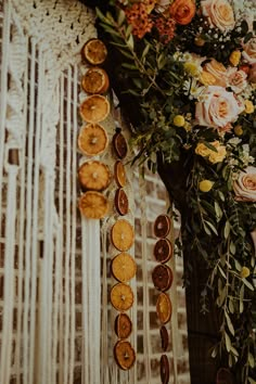 an arrangement of oranges and flowers on display in front of a wall with fringe