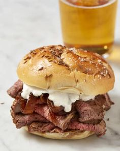 a roast beef sandwich with sour cream on it and a glass of beer in the background