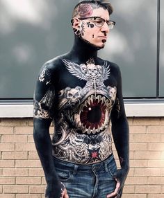 a man with tattoos on his body standing in front of a brick wall and window