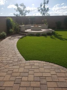 a brick path leads to a circular fountain in the middle of a grassy lawn area