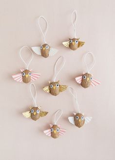 six wooden ornaments with eyes and wings hanging from strings on a pink background, top view