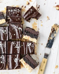 there are many pieces of chocolate cake on the table next to a knife and fork